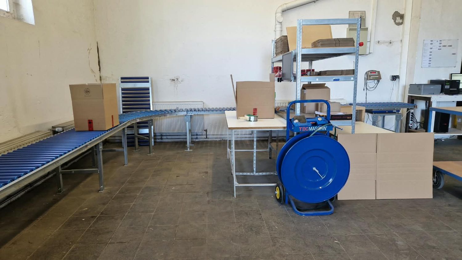 Packbereich der Halle mit Rollenbahnen, Packtischen und bereitstehenden Kartons
