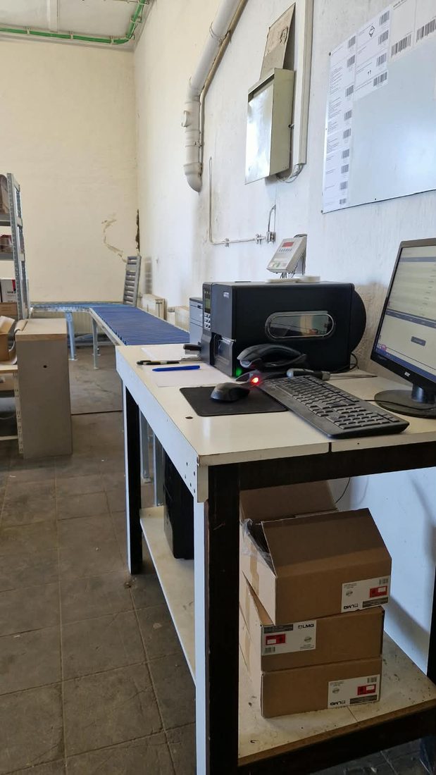 Packtisch mit Monitor, Tastatur und Scanner, daneben gefaltete Versandkartons